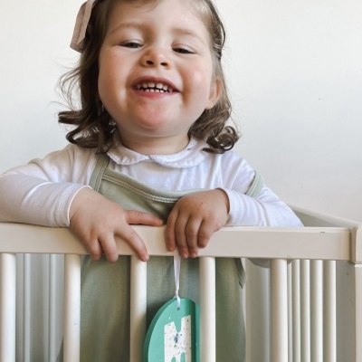 Criança sorridente no berço branco com pendente verde com letra M