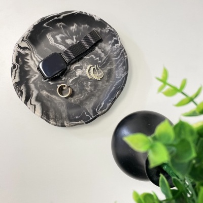 Prato decorativo com relógio e anéis ao lado de planta verde