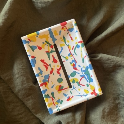 Caixa retangular colorida com padrão de manchas coloridas sobre tecido cinza