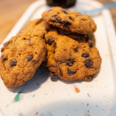 Bandeja com quatro bolachas tipo cookies com pepitas de chocolate e um copo de café ao fundo