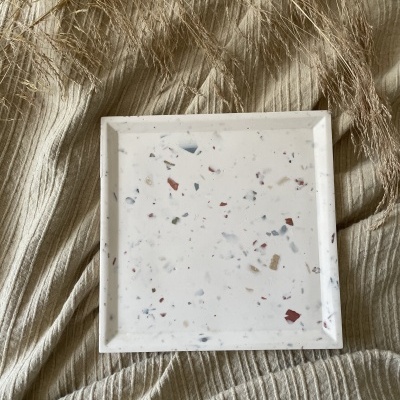 Prato quadrado branco com padrão terrazzo sobre tecido creme texturizado