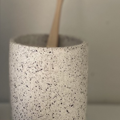 Vaso cerâmico branco com manchas pretas e escova de dentes de madeira