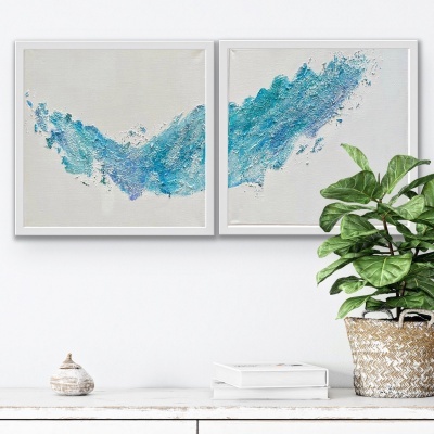 Duas pinturas abstratas azuis em molduras brancas sobre uma parede branca com uma planta verde ao lado.