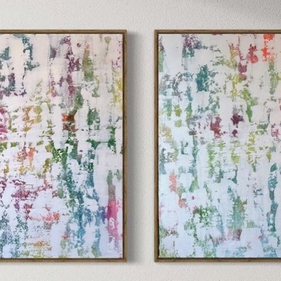 Dois quadros abstratos coloridos com moldura dourada pendurados numa parede branca.