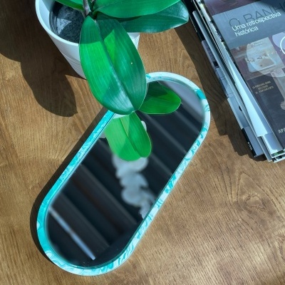 Trilho de mesa oval com borda azul e branca, planta verde em vaso branco e revistas sobre mesa de madeira