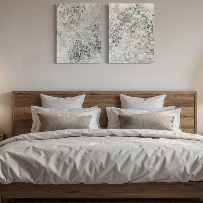 Cama de madeira clara com roupa de cama branca e almofadas bege e branca, duas telas abstratas cinzentas na parede.