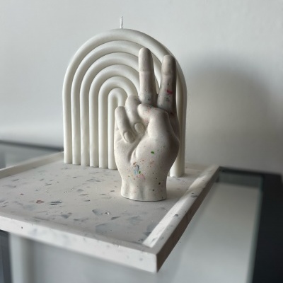 Vela decorativa branca em forma de mão com manchas coloridas sobre base marmorizada branca com arco decorativo