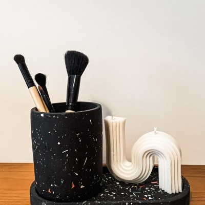 Suporte preto com pincéis de maquilhagem e vela decorativa branca abstrata