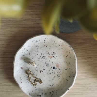 Prato pequeno redondo de cerâmica com padrão salpicado sobre mesa de madeira clara e ramo amarelo desfocado