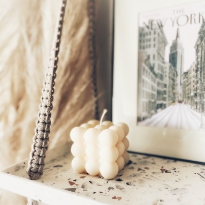 Vela cubo creme com esferas sobre prateleira de mármore com quadro do Empire State Building