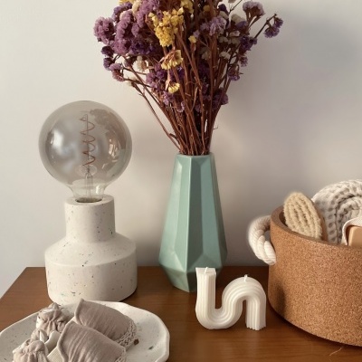 Conjunto decorativo com abajur, vaso com flores secas, vela curva, cesta de cortiça com toalhas e chinelos cinza