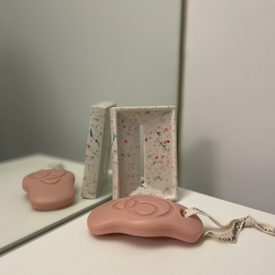 Dispositivo cor-de-rosa com cordão branco junto a caixa pontilhada colorida sobre superfície branca e espelho.