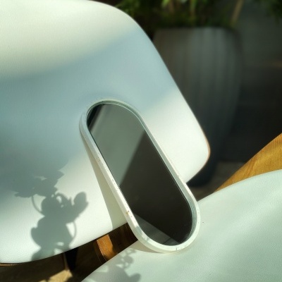 Espelho oval com moldura branca sobre cadeira branca de plástico próximo a planta