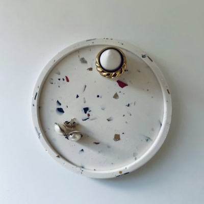 Prato de mármore branco com manchas coloridas e joias colocadas em cima.