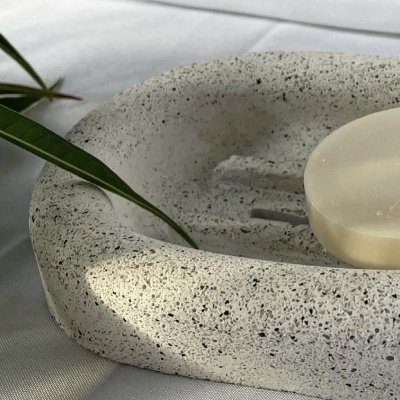 Saboneteira de pedra cinzenta com sabonete branco em tecido branco e folha verde