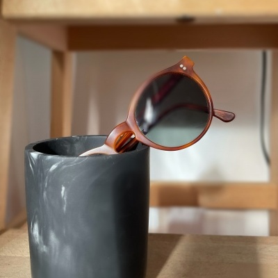 Óculos de sol castanhos dentro de copo preto sobre mesa de madeira.