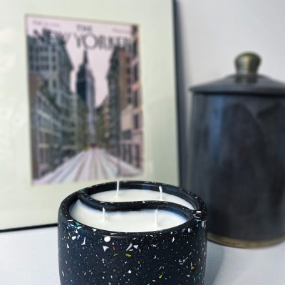 Vela em recipiente preto com padrão terrazzo e quatro pavios numa mesa branca