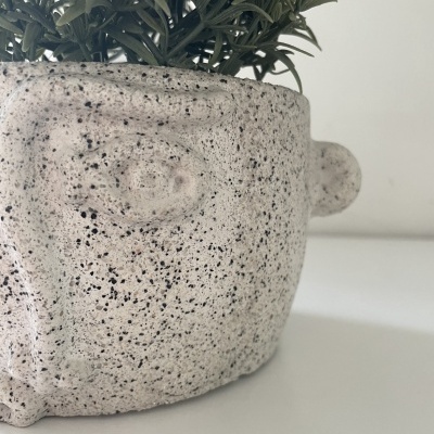 Vaso cerâmico estilizado em forma de rosto com planta artificial verde