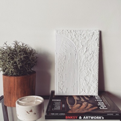 Quadro branco texturizado, revistas, vaso de madeira com planta e recipiente branco