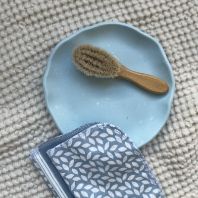 Escova de madeira com cerdas sobre prato azul claro e tecido azul com padrão branco