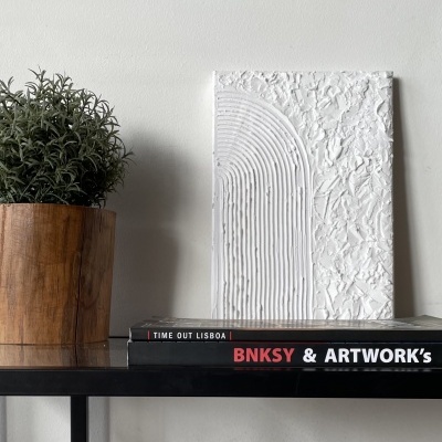 Prateleira com livros, vaso de madeira com planta e objeto decorativo branco texturizado