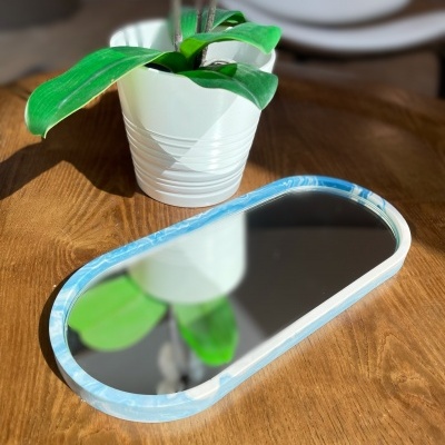 Espelho oval com moldura azul e branca ao lado de vaso branco com planta verde