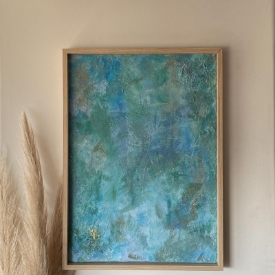 Quadro decorativo abstrato em azul e verde com moldura de madeira na parede bege e ramo seco junto.