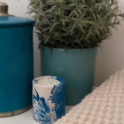 Vela marmoreada azul e branca com vaso e planta ao fundo