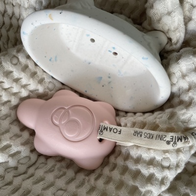 Barra de sabão rosa e esponja branca com manchas azuis sobre tecido branco texturizado