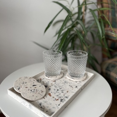 Conjunto de tabuleiro e porta-copos em pedra terrazzo com dois copos de vidro texturado sobre mesa branca redonda