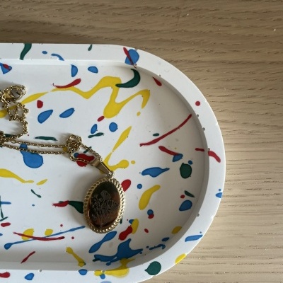 Tabuleiro branco com manchas coloridas e colar dourado com pendente oval preto em cima de madeira clara