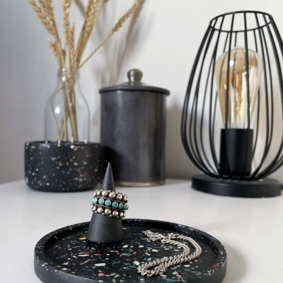 Suporte redondo preto com padrão colorido com anéis e corrente, vaso com plantas secas, jarro preto e lâmpada decorativa