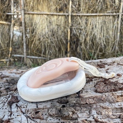 Saboneteira com sabonete rosa sobre tronco de árvore com parede de palha ao fundo