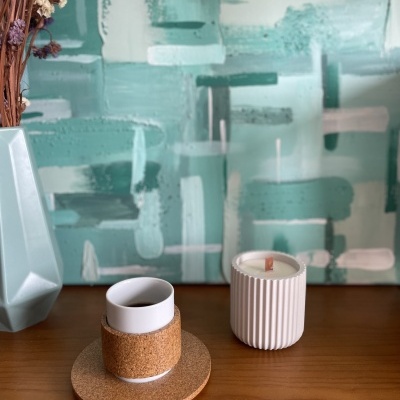 Vaso azul, copo em cortiça, vela branca e fundo artístico verde e branco