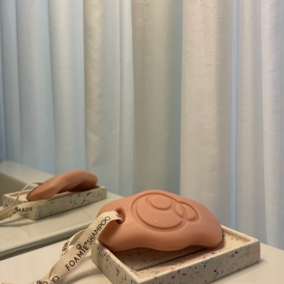 Telefone vintage cor de rosa com cordão branco com texto FOAMIE.SHAMPOO sobre caixa branca com padrões multicoloridos num tampo com espelho e cortinas brancas