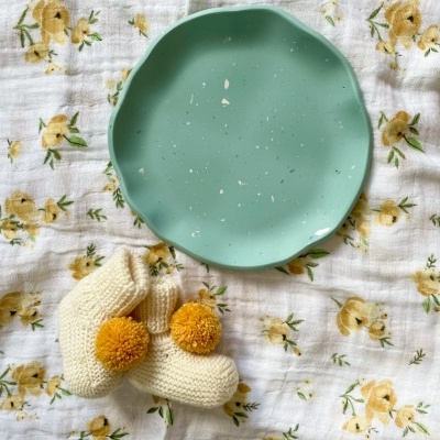 Prato verde de cerâmica com meias de malha e pompons sobre tecido floral