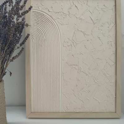 Quadro decorativo bege com textura e padrão de arcos em relevo ao lado de ramo seco de flores roxas