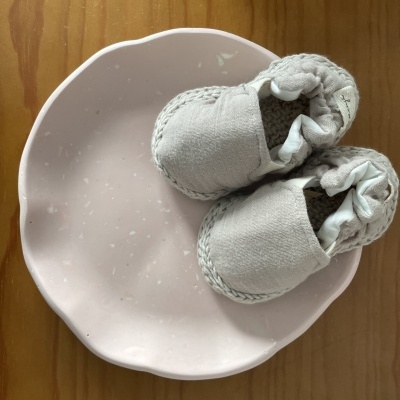 Sapatinhos brancos sobre prato rosa claro numa mesa de madeira