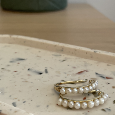Brincos de argola dourados com pérolas sobre bandeja creme texturizada