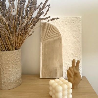 Conjunto decorativo com vaso, relevo artístico, vela cubo e escultura de mão em cima de móvel de madeira