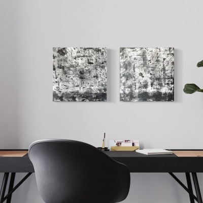 Espaço de trabalho minimalista com secretária preta, cadeira preta, planta verde e duas telas abstratas cinza na parede