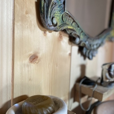 Sabonete marrom em suporte branco de sabonete numa prateleira de madeira ao lado de espelho com moldura ornamentada.