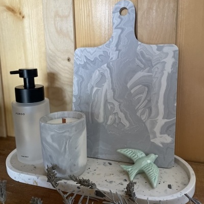 Conjunto decorativo com tábua marmoreada, vela, dispensador TORSO, bandeja branca manchada e figura de pássaro verde