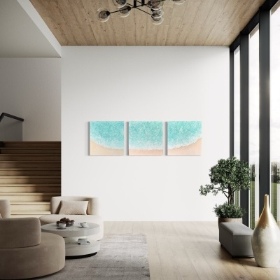 Sala de estar moderna com sofá bege, mesa de centro branca, quadro triptico de praia e oceano, e vaso com planta ao lado da janela