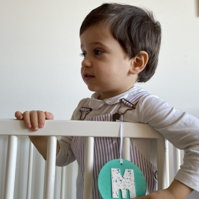 Criança com brinquedo verde com letra M pendurado em berço branco