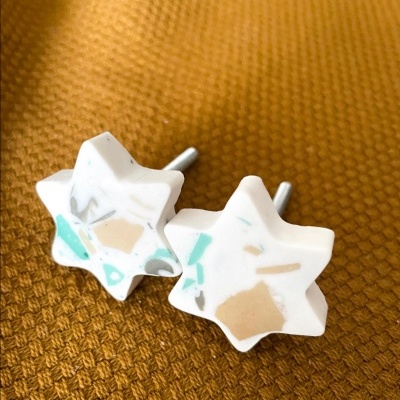 Brincos estrela de resina branca com manchas em bege e verde, pino metálico, em fundo castanho