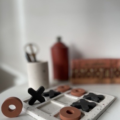 Jogo da velha em madeira com peças pretas e castanhas num tabuleiro branco sobre superfície branca