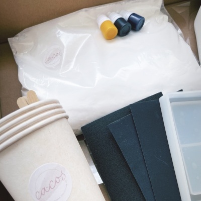 Kit de artesanato com copos de papel, tintas, folhas pretas e bandeja de silicone dentro de caixa de cartão