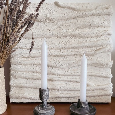 Dois castiçais de mármore com velas em fundo texturizado e arranjo floral seco