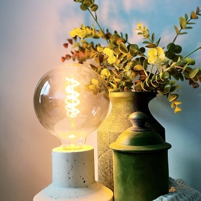 Lâmpada com base branca, vaso com folhas verdes, frasco verde e manta branca